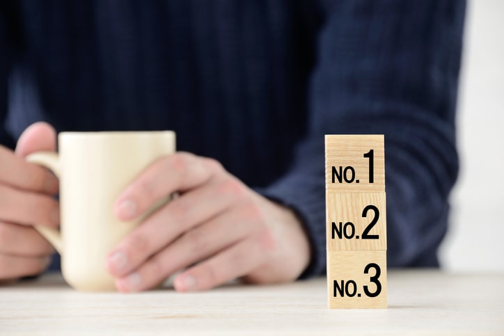 A person in a dark sweater holds a beige mug, with wooden blocks numbered 1, 2, and 3 stacked on a table. The setting resembles an informal meeting with franchise consultants offering expertise and guidance.